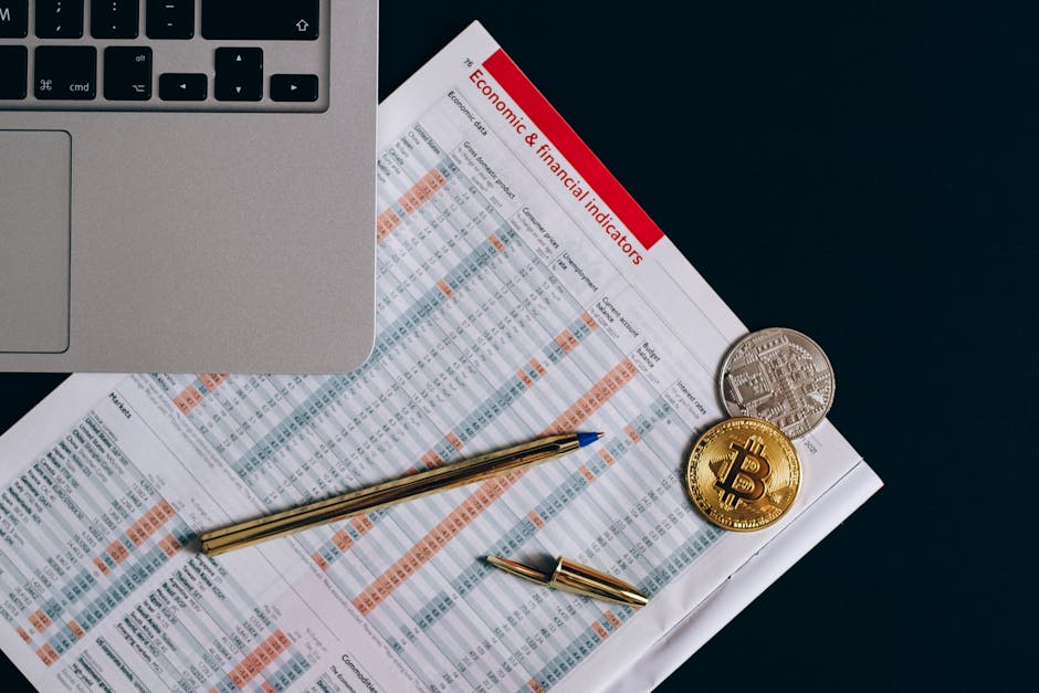 Top view of bitcoin coins on financial documents beside a laptop keyboard.